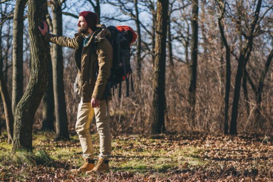 homme hipster voyageant avec sac à dos dans la forêt d'automne portant veste chaude, chapeau, touriste actif, découverte de la nature en saison froide