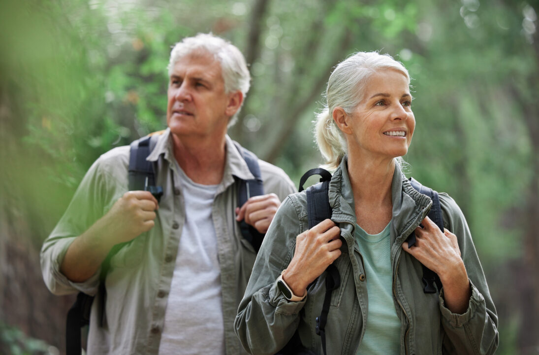 Couple de seniors en pleine randonnée en forêt, souriants et actifs, profitant de la nature pour un mode de vie sain à la retraite