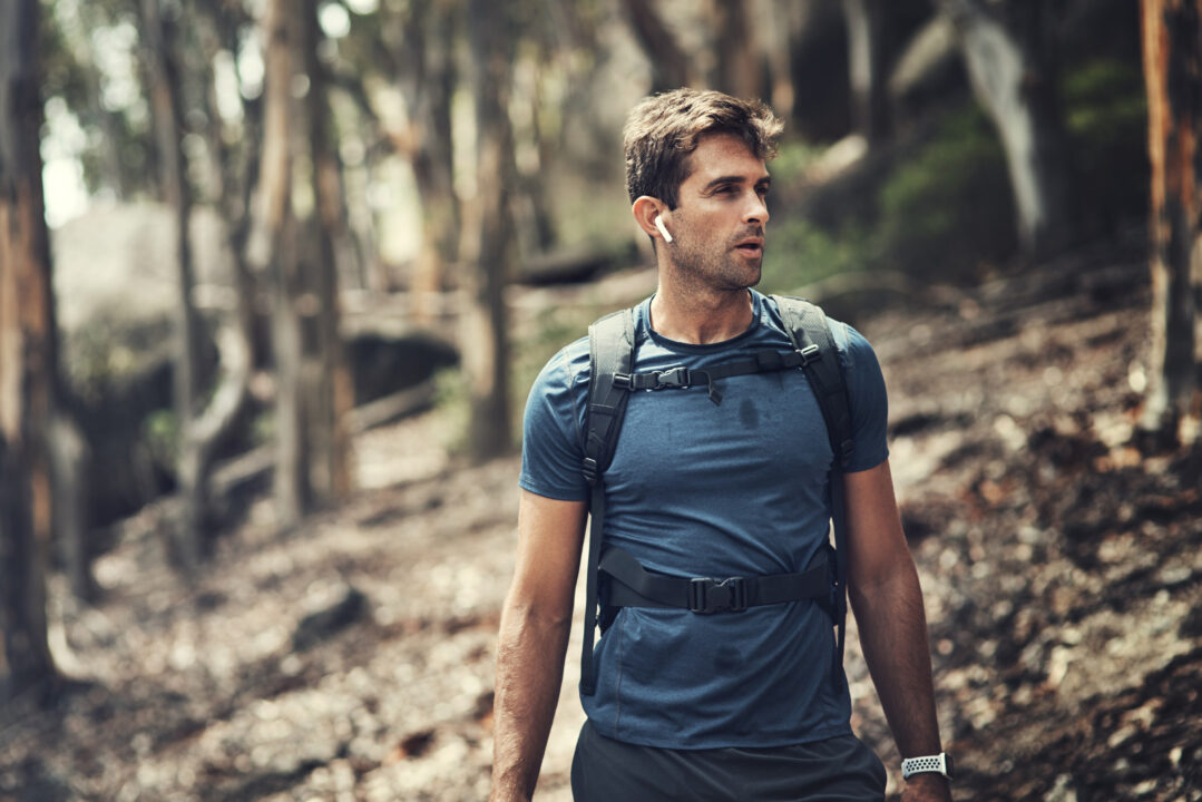 Homme en rucking marchant en forêt avec écouteurs, séance de fitness en plein air