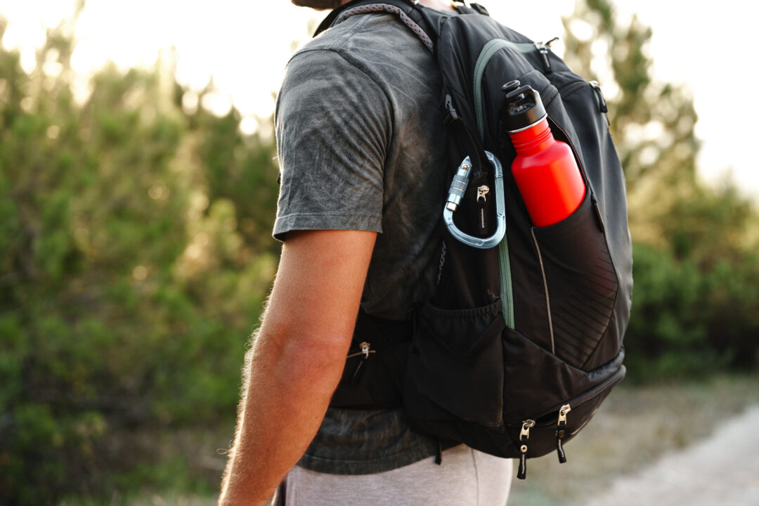 a male traveler backpack with mountaineering carabiner and thermos close up