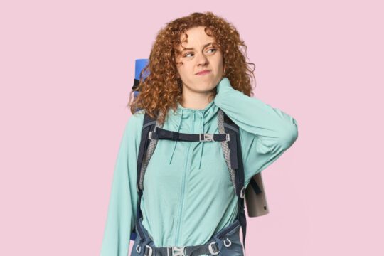 Jeune randonneur roux touchant son dos en ressentant une douleur lors d’une marche avec sac à dos lesté